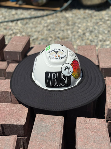 An all-black sunshade with a white hard hat featuring text and logo, and stickers placed on a stack of bricks.