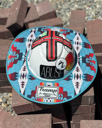 a turquoise sunshade with red, yellow, white and navy accents from tramp life industries on a white hard hat with tramp life stickers sitting on a pile of bricks
