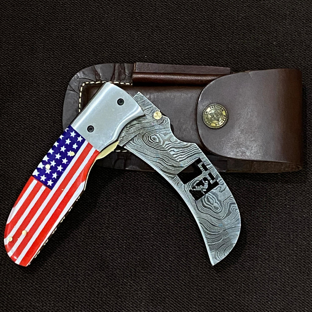 Folding knife with American flag handle in leather sheath on black background