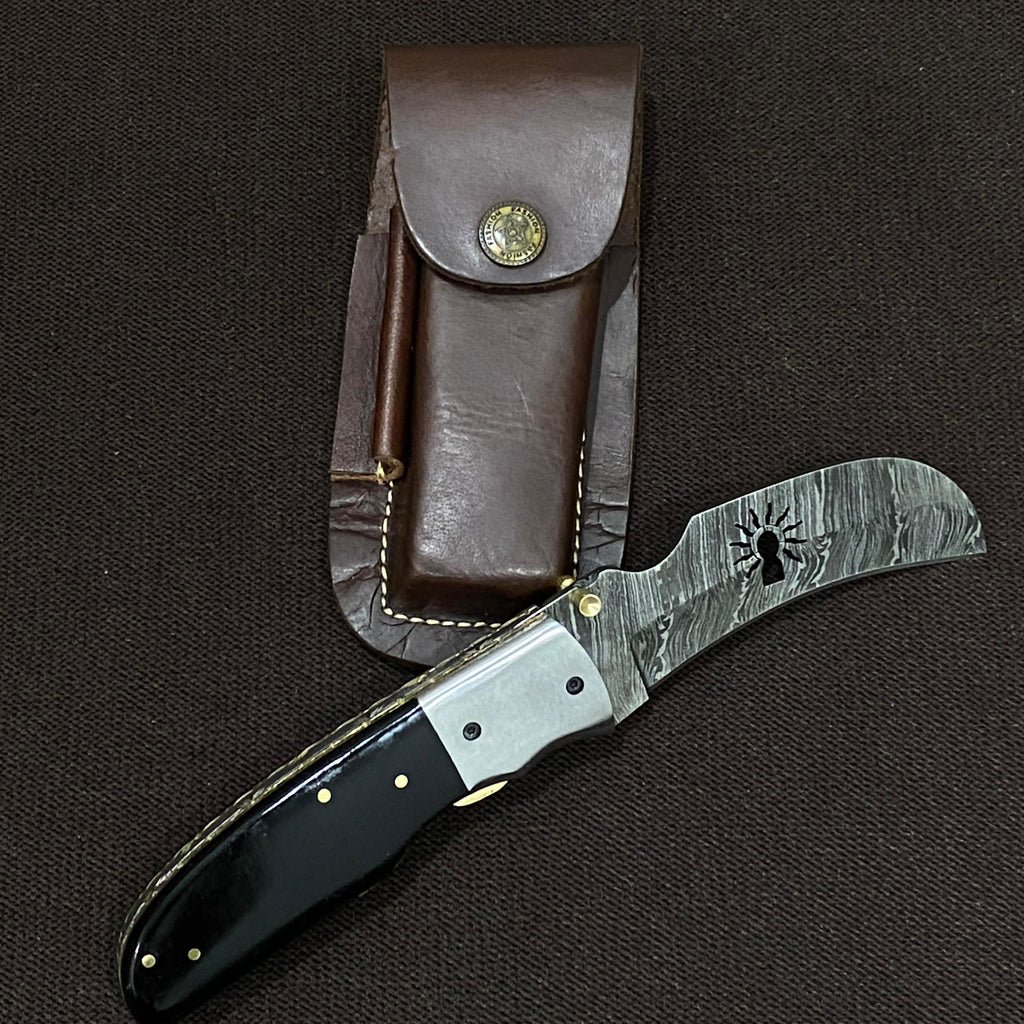 damascus steel knife with black handle on a dark background. has the ibew hand logo etched out in the middle of the blade.