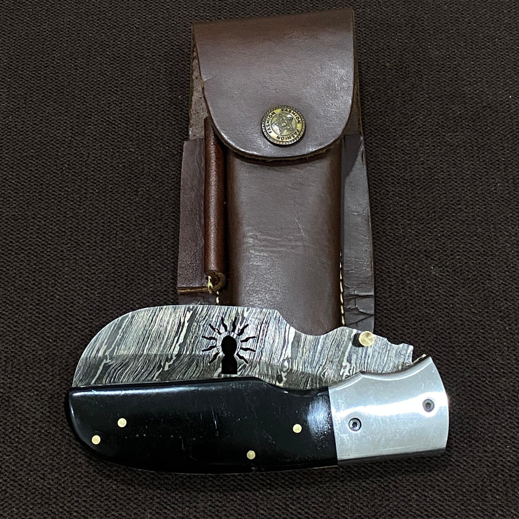 a folded up damascus steel knife with a black handle next to a dark leather sheath