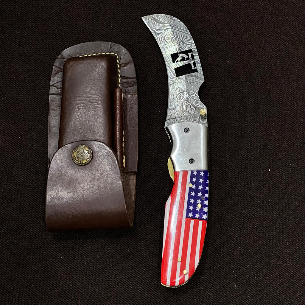 Folding knife with American flag handle and leather sheath on a black background