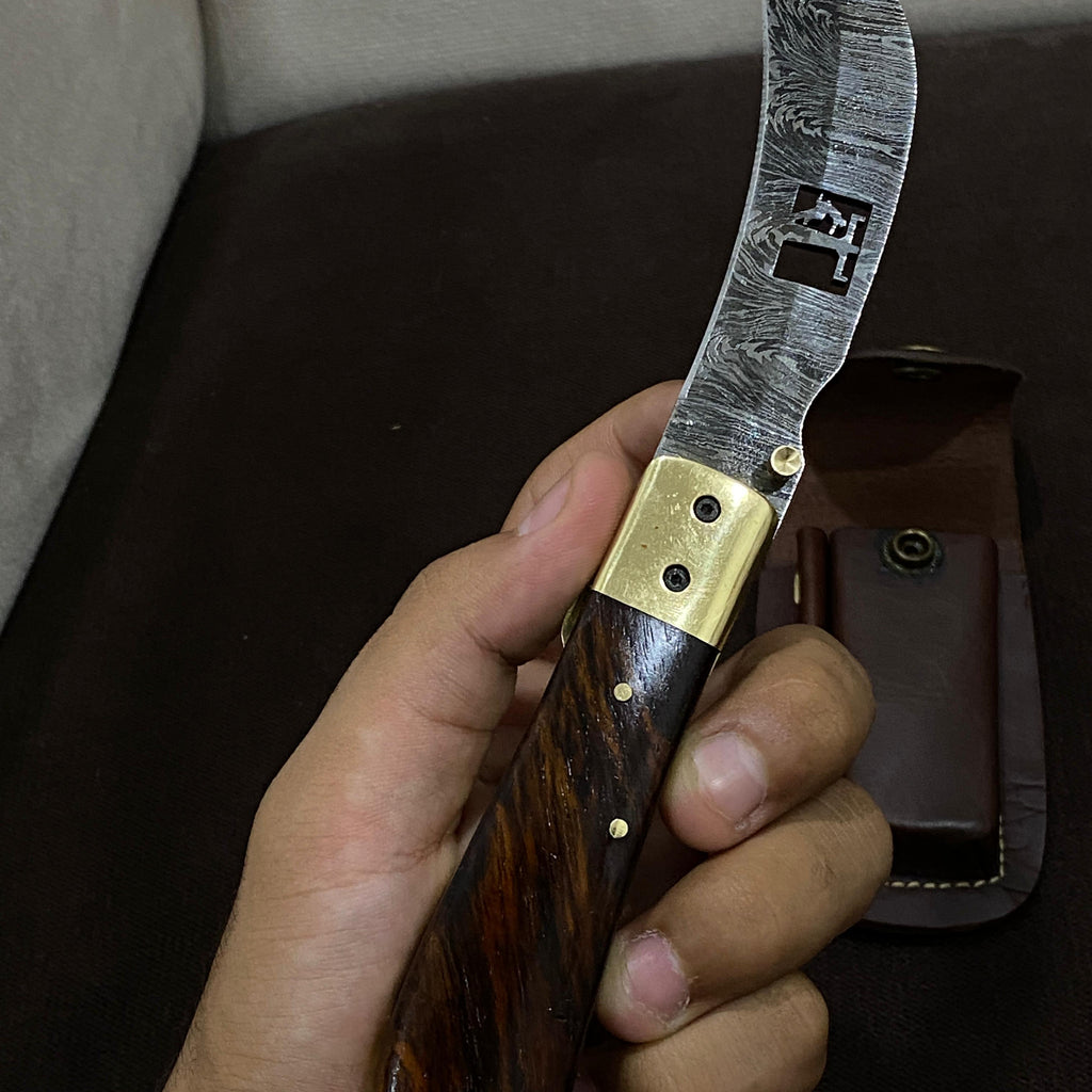 hand holding foldable damascus steel hawskbill knife with a lineman etched out of the blade.