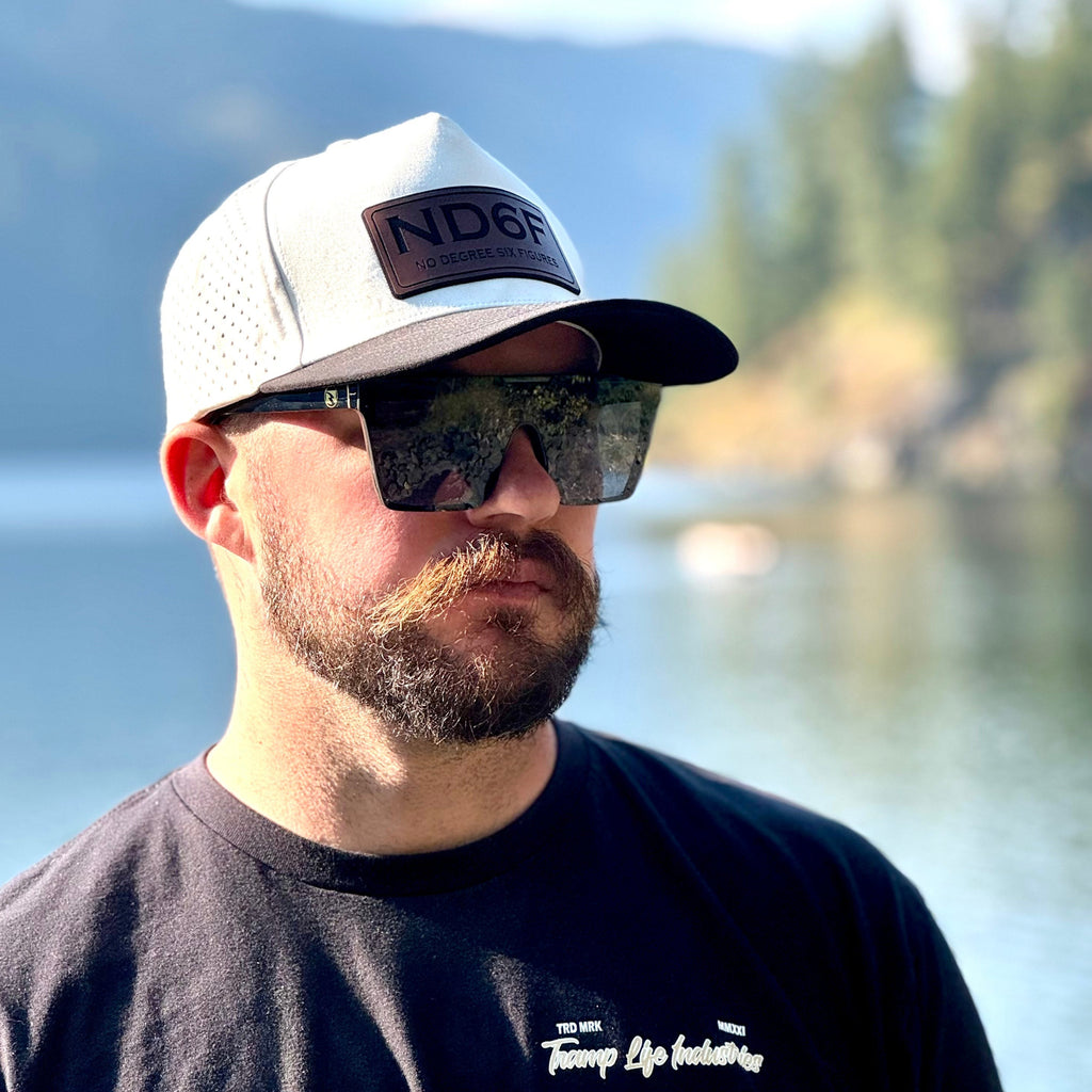 Man wearing a water resistant hat from tramp life that says ND6F and sunglasses with a scenic background