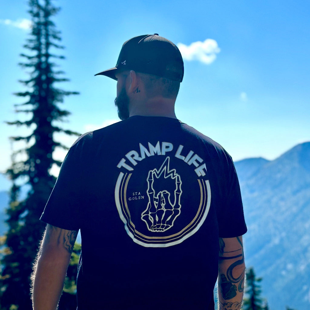 man standing with the stay golden shirt from tramp life. mountains and trees in background
