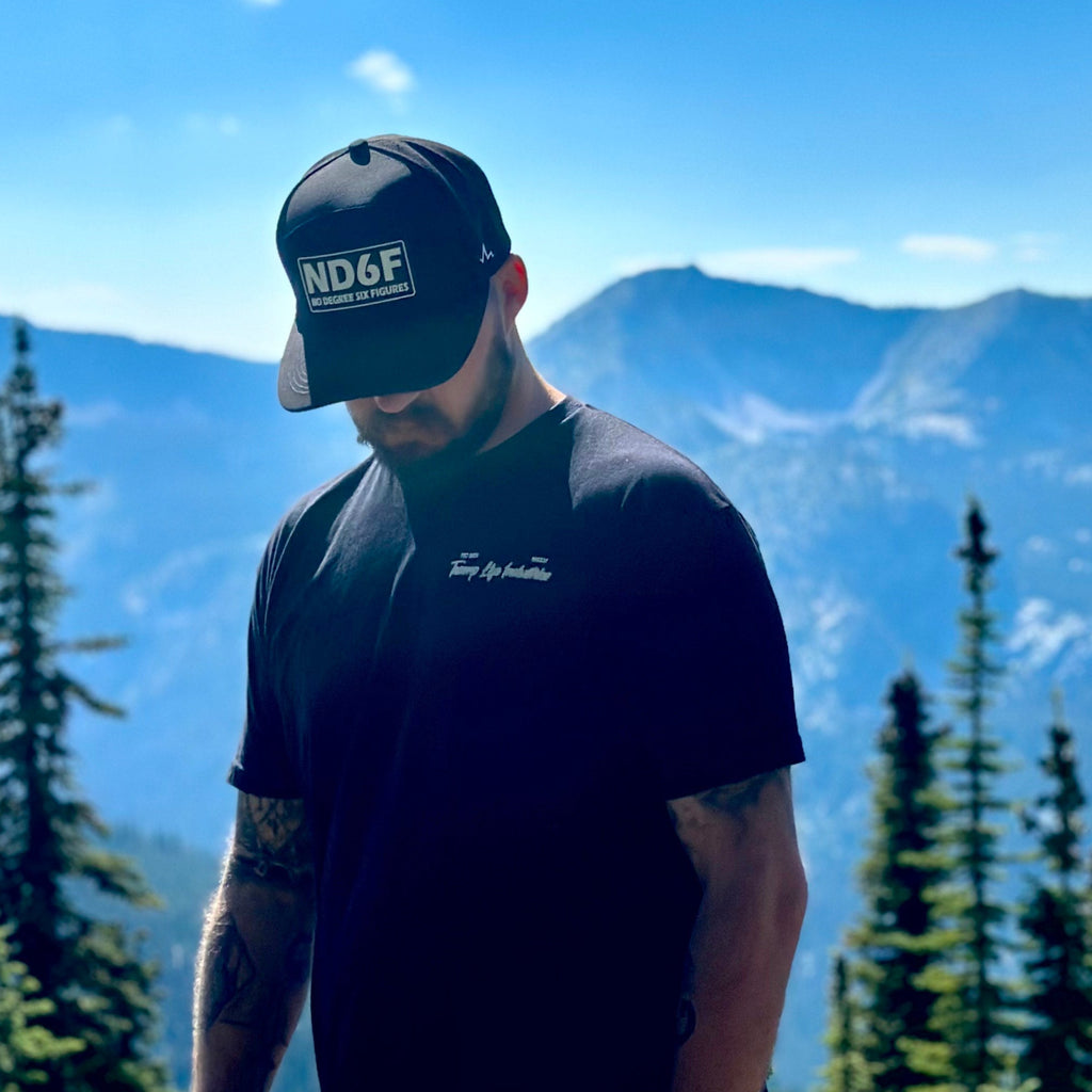 man standing in front of trees and mountains with the front of the stay golden shirt from tramp life