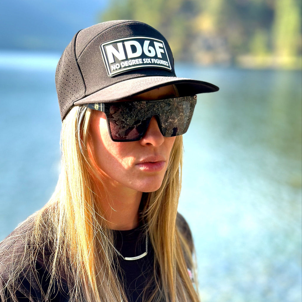 Person wearing a black cap with 'NDGF' logo and sunglasses, standing by a lake.