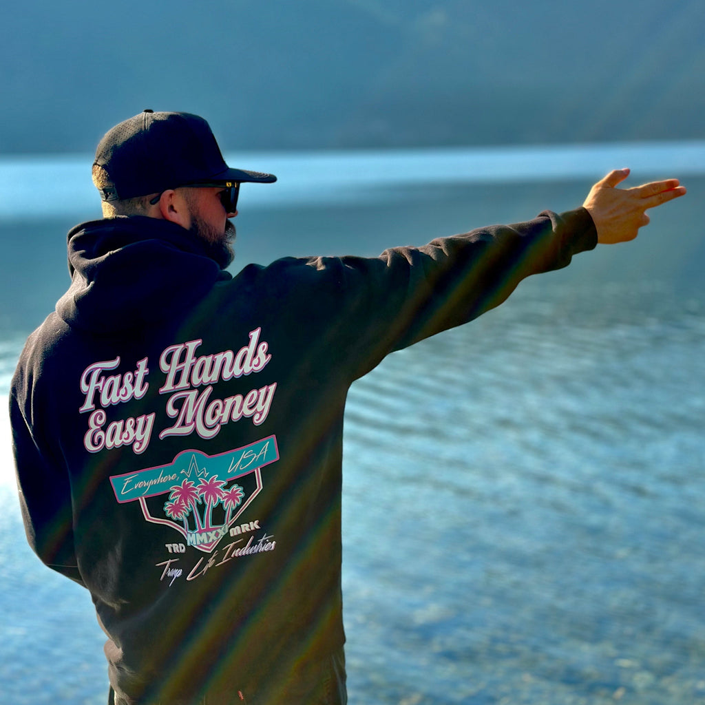 man standing next to water with a hoodie from tramp life that says fast hands easy money in miami vice colors