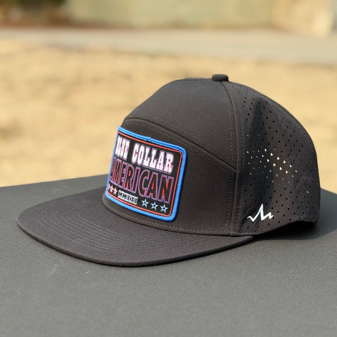 black flat bill hat that says blue collar american with red white and blue colors on a black table