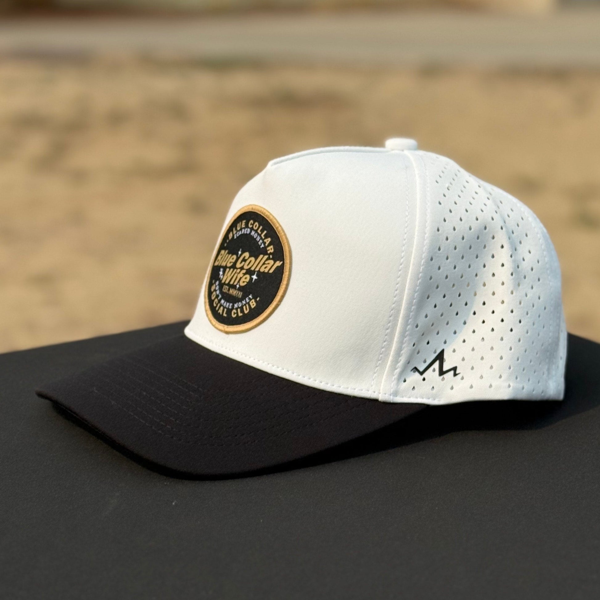 White and black cap with a logo on a black surface. hat says blue collar wife social club