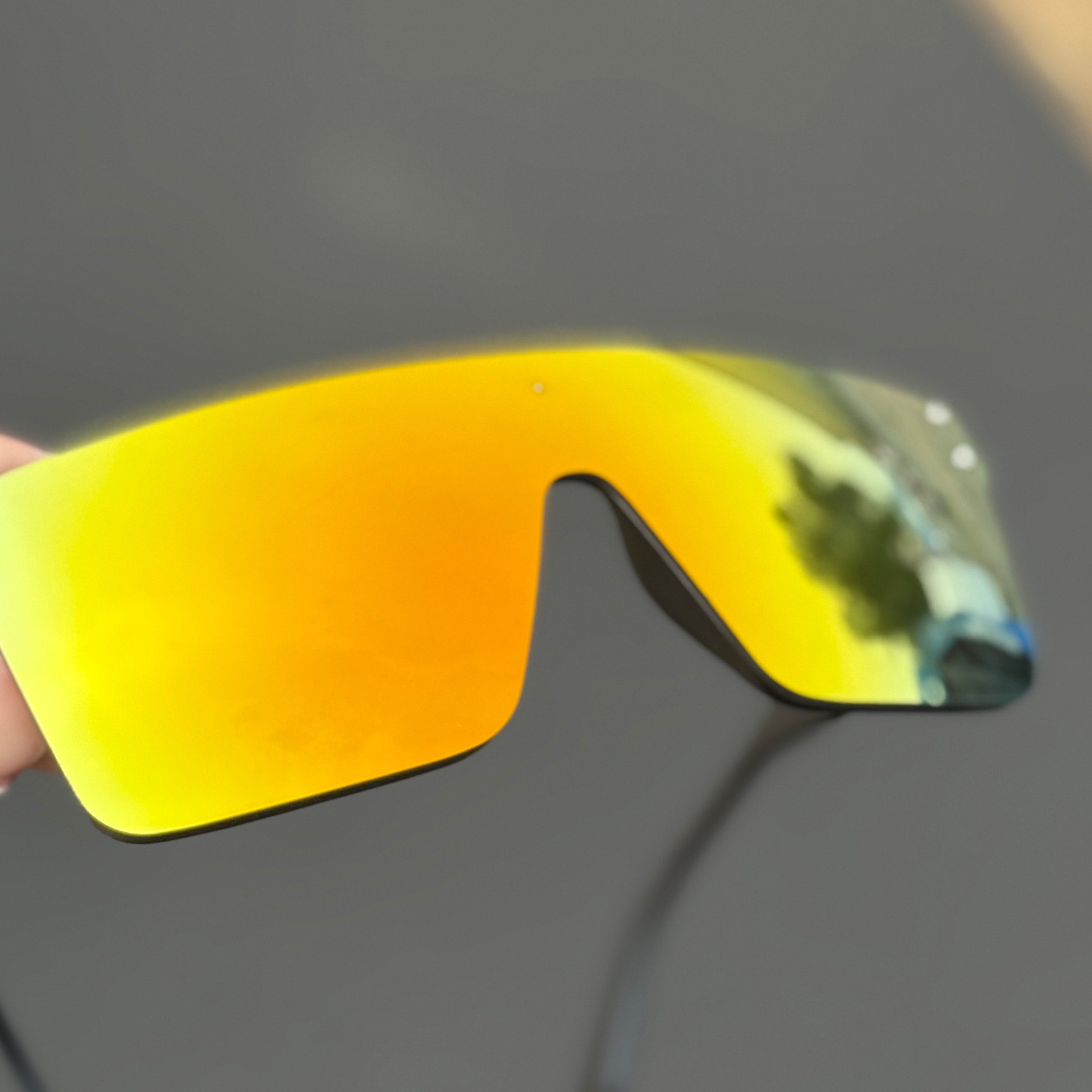 Yellow reflective sunglasses held by a hand with a blurred background
