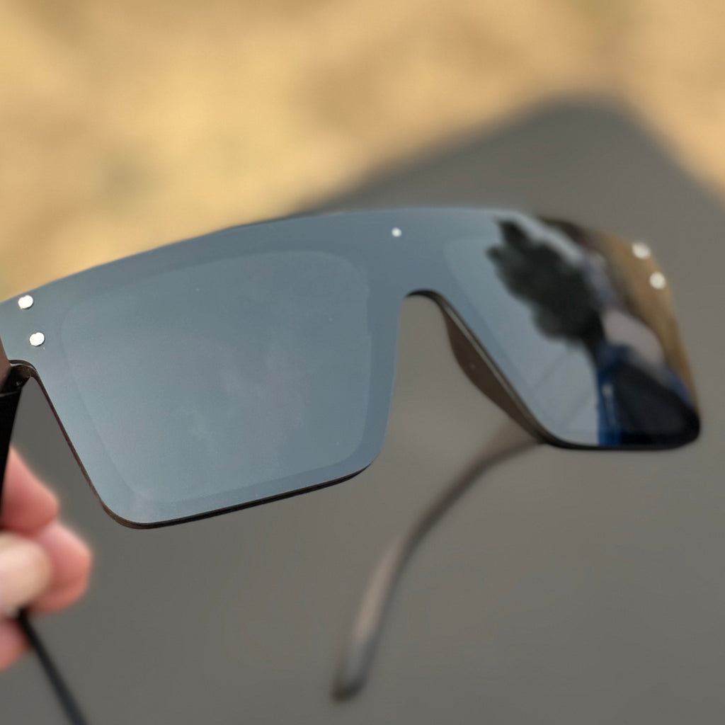 Black sunglasses held by a hand with a blurred natural background