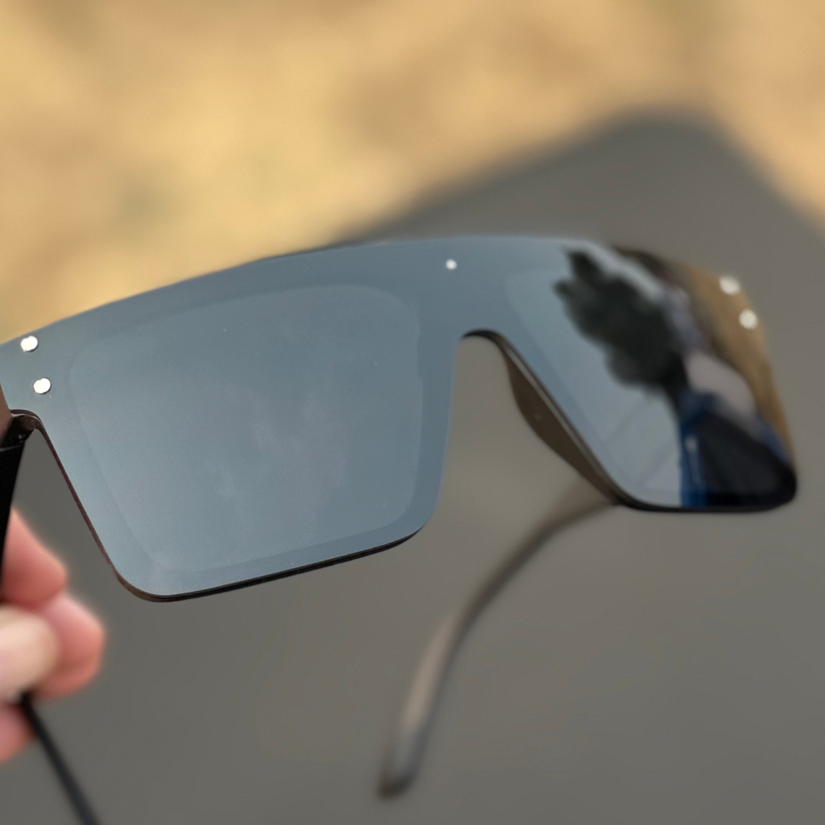 Black sunglasses held by a hand with a blurred natural background