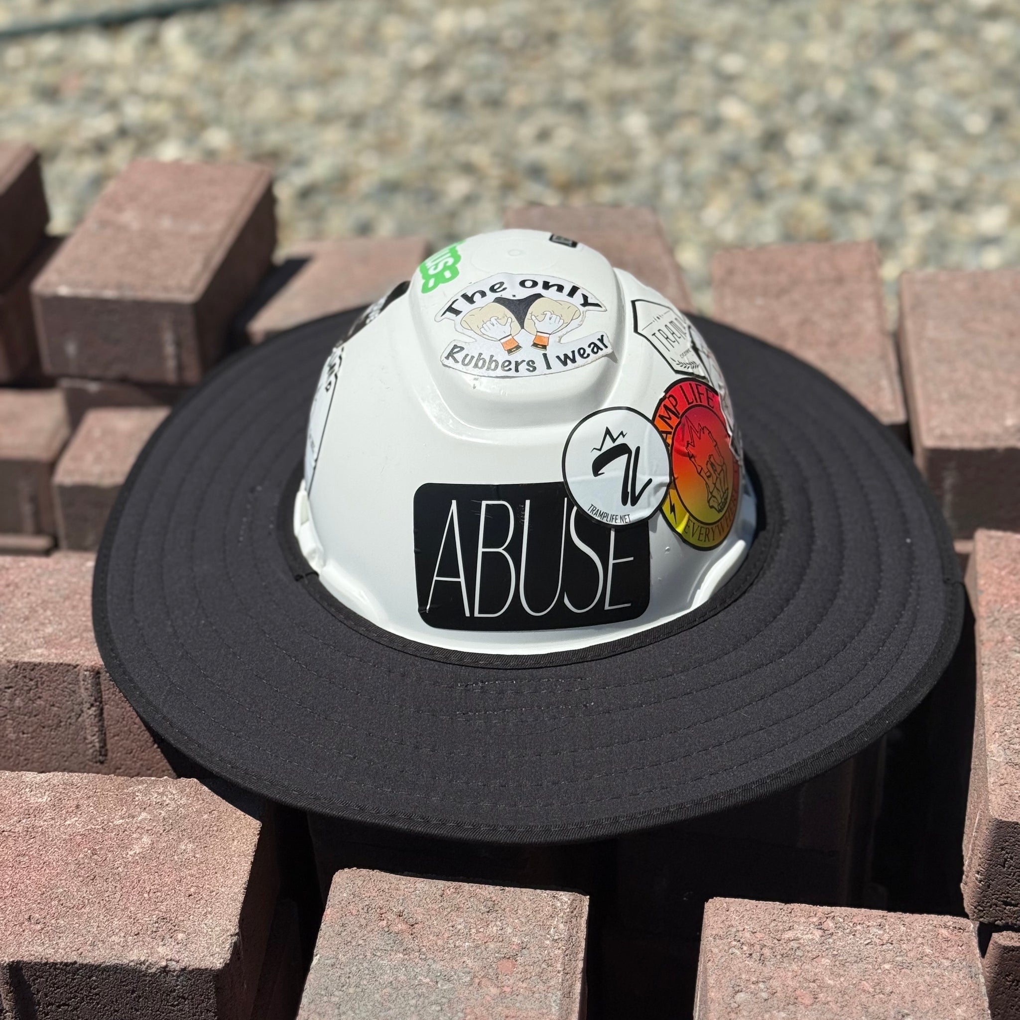 An all-black sunshade with a white hard hat featuring text and logo, and stickers placed on a stack of bricks.