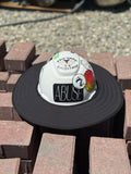 An all-black sunshade with a white hard hat featuring text and logo, and stickers placed on a stack of bricks.