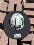 An all-black sunshade from tramp life industries with a PVC patch sewn into it with the words TRAMP on a white hard hat with tramp life stickers