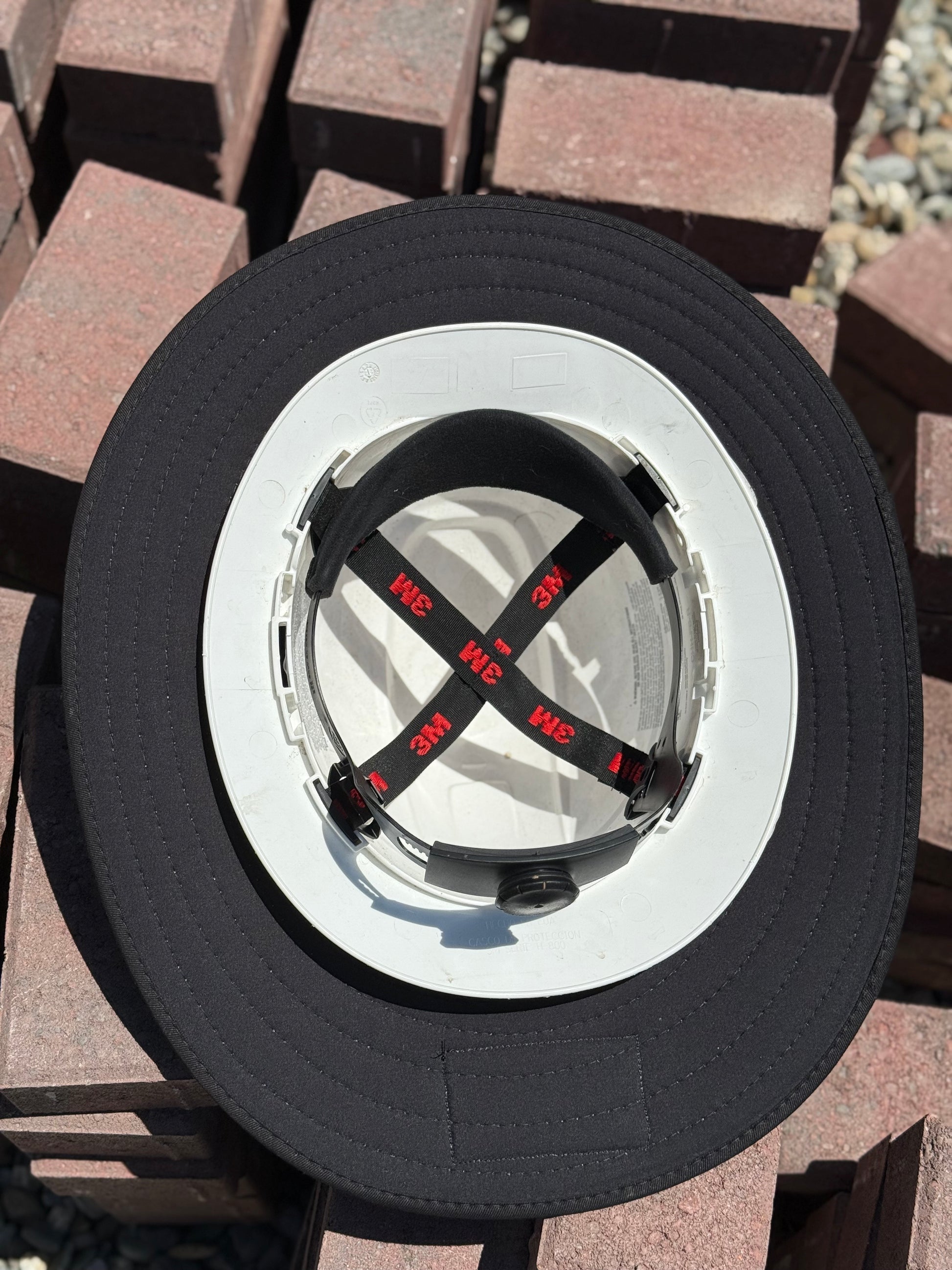 a close up of an all black sunshade on a white hard hat turned upside down showing the inside of the hard hat