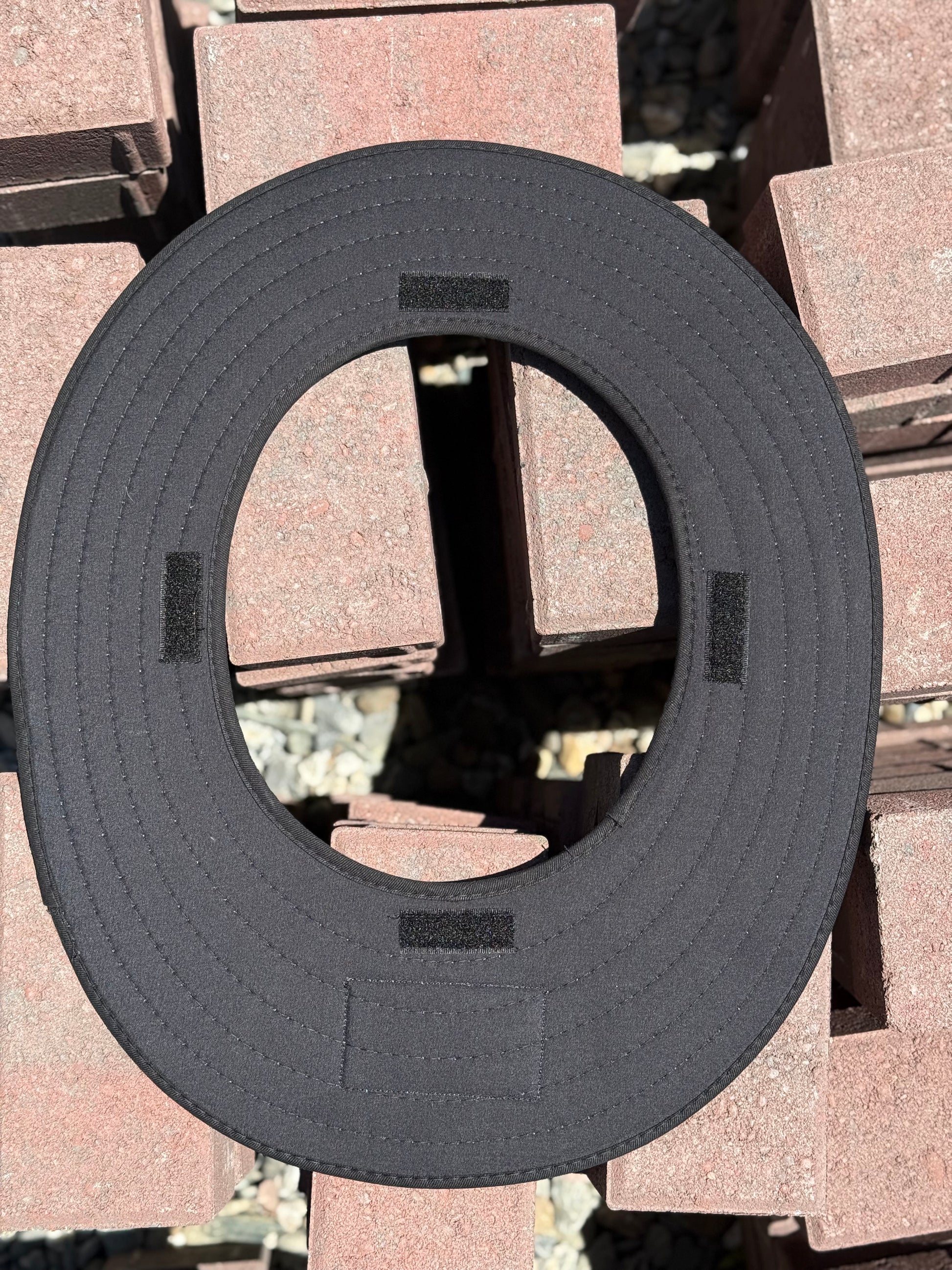 an all black sunshade made for a hardhat upside down showing the velcro that is sewn into the bottom of it showing where it attaches to a hard hat