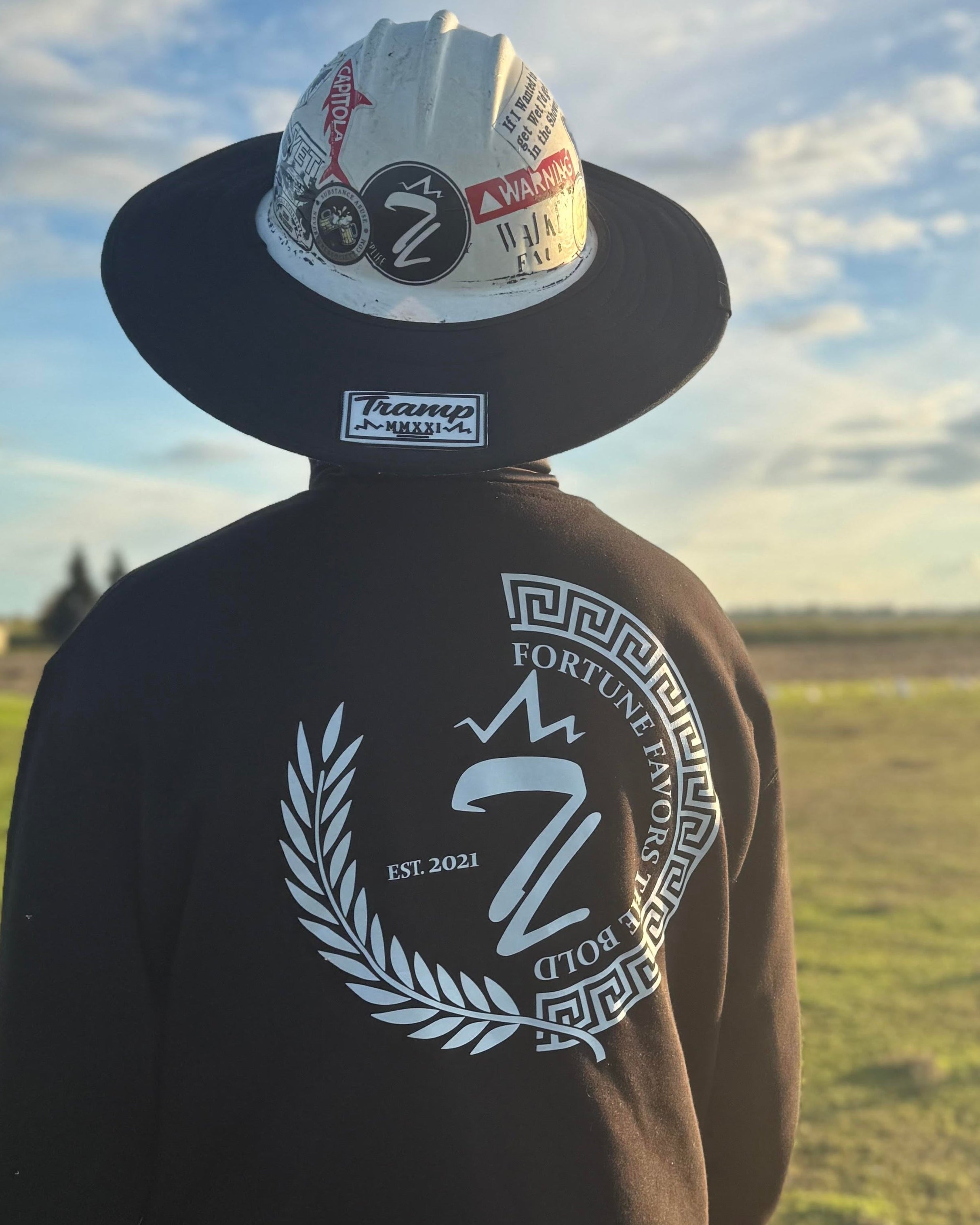 person wearing a the duality crew neck sweatshirt from tramp life industries. a blue collar work sweatshirt that is black with a white laurel on the left side, a white greek key half circle on the right and the iconic TL from tramp life in the center. around the inside of the circle it also says "fortune favors the bold"