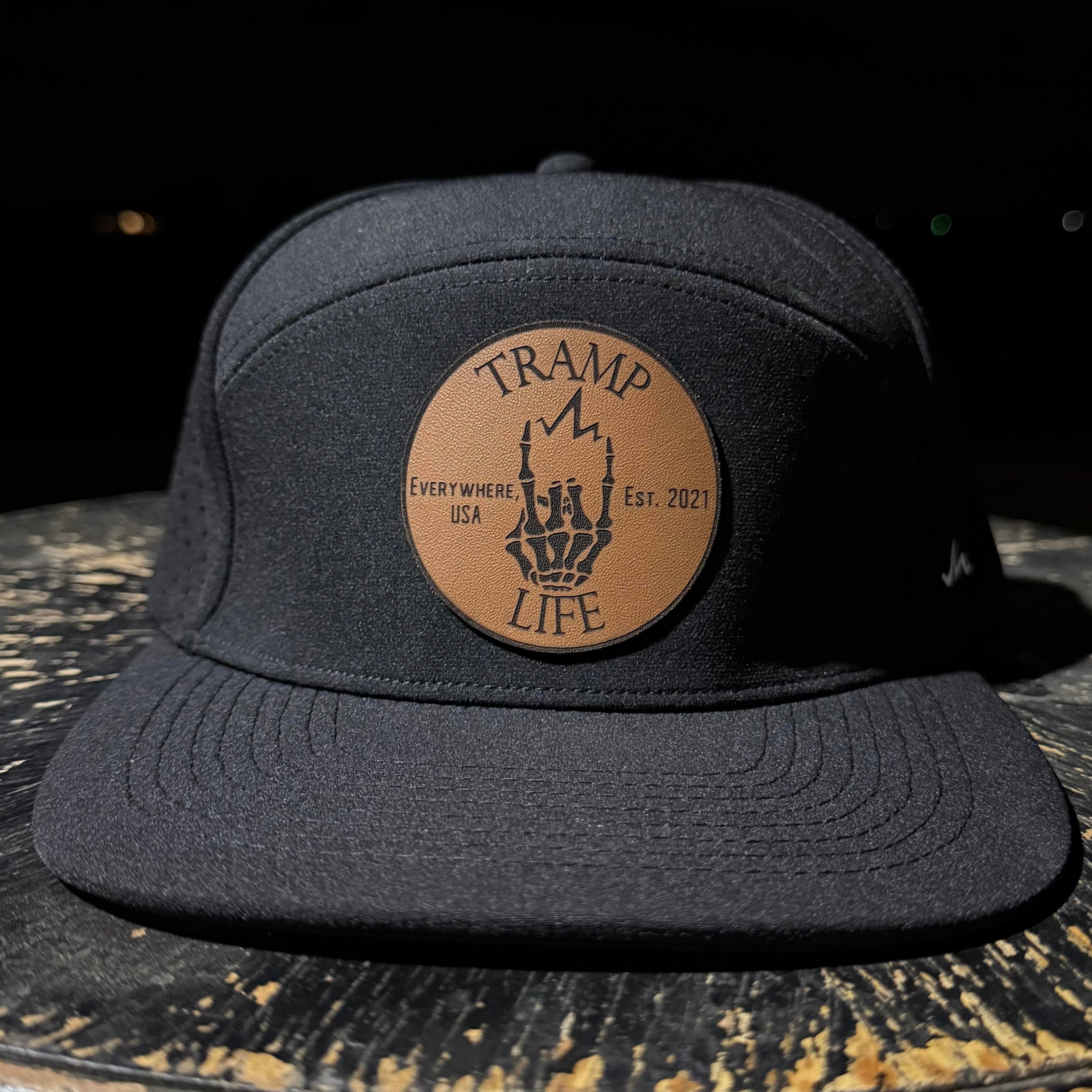 Black cap with a brown leather patch that says tramp life on a dark surface