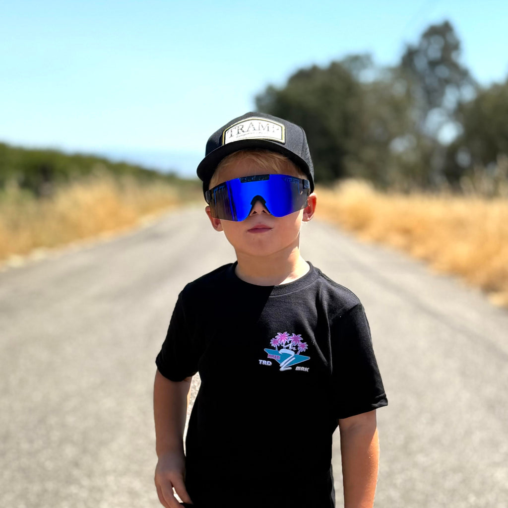 Child wearing sunglasses and a black tramp life t-shirt with palm trees on a road with trees in the background