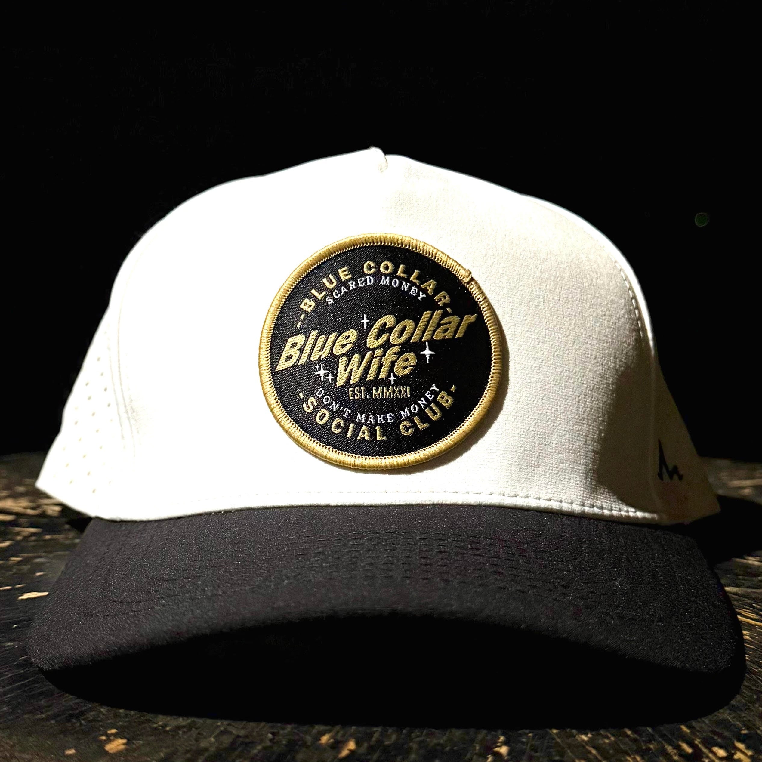 White cap with a 'Blue Collar Wife' patch on a dark background