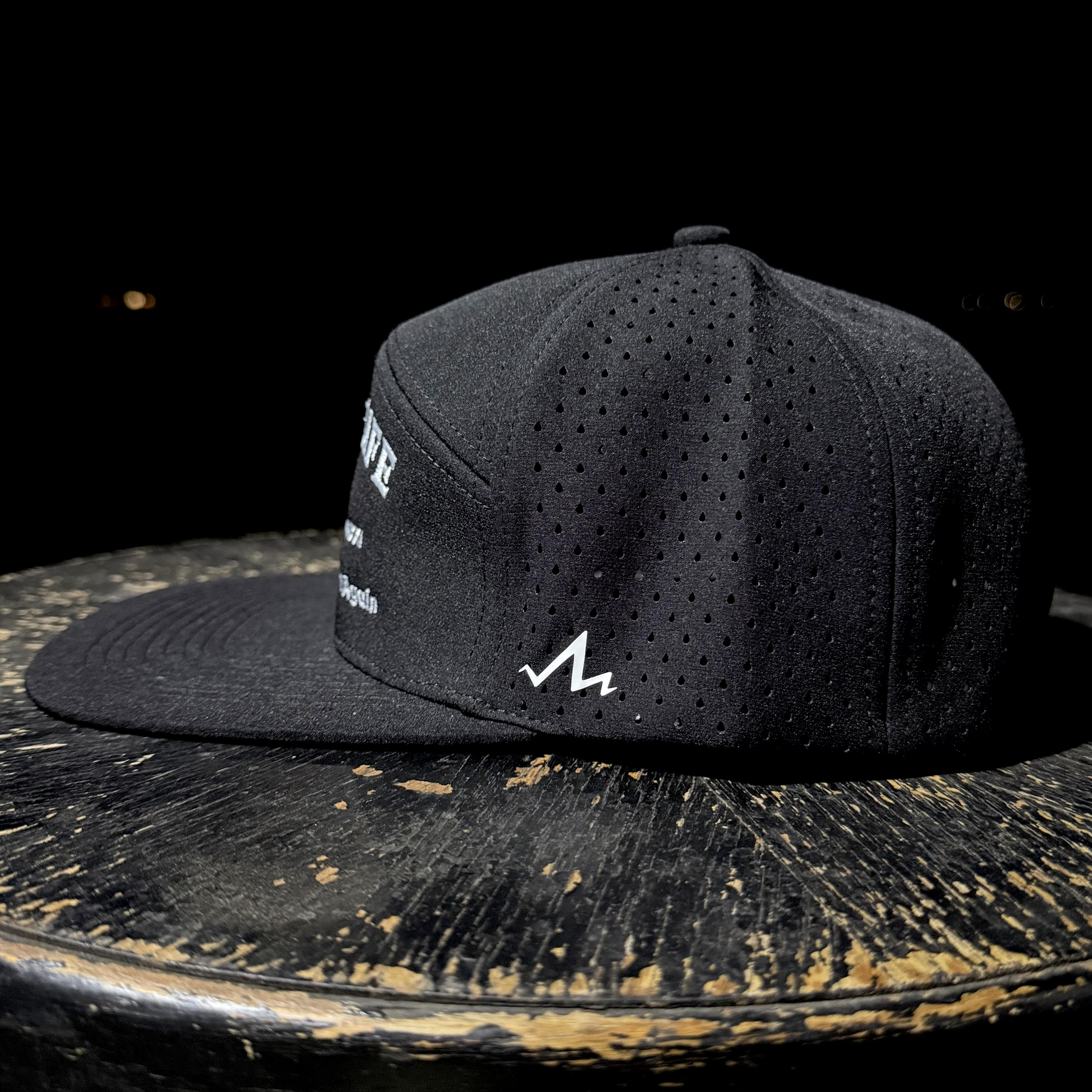 Black cap with white text and logo on a wooden surface