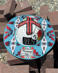 a turquoise sunshade with red, yellow, white and navy accents from tramp life industries on a white hard hat with tramp life stickers sitting on a pile of bricks