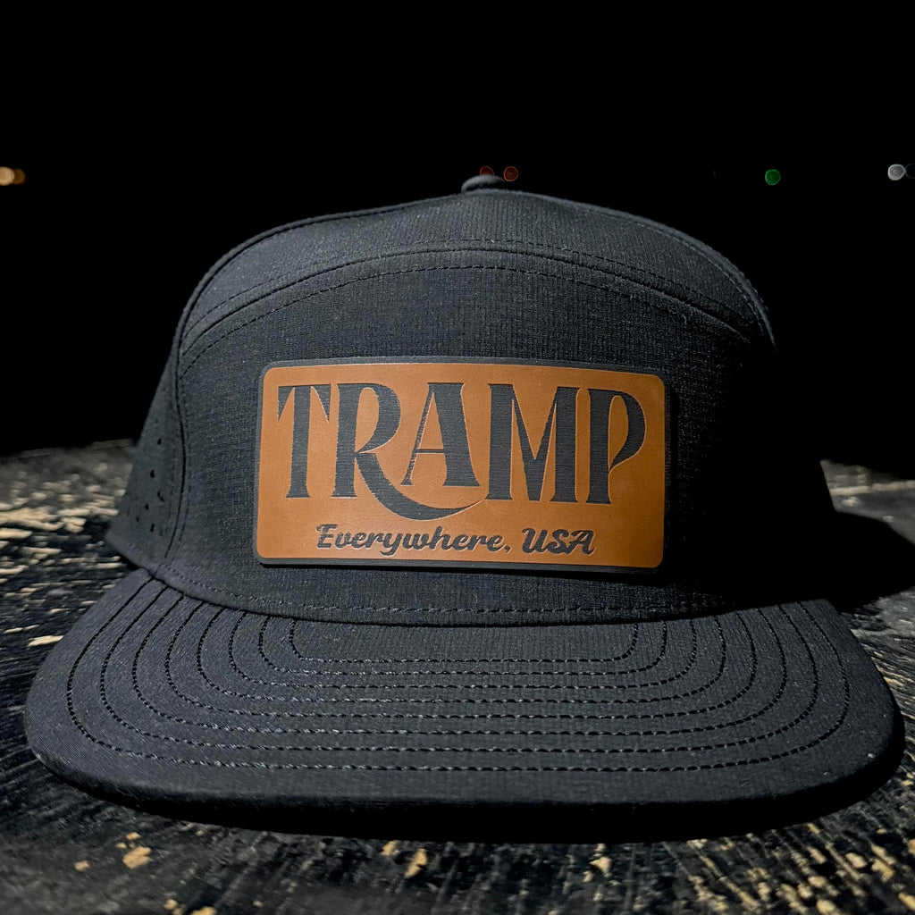 Black cap with a brown leather patch displaying 'TRAMP Everywhere USA' on a dark background.
