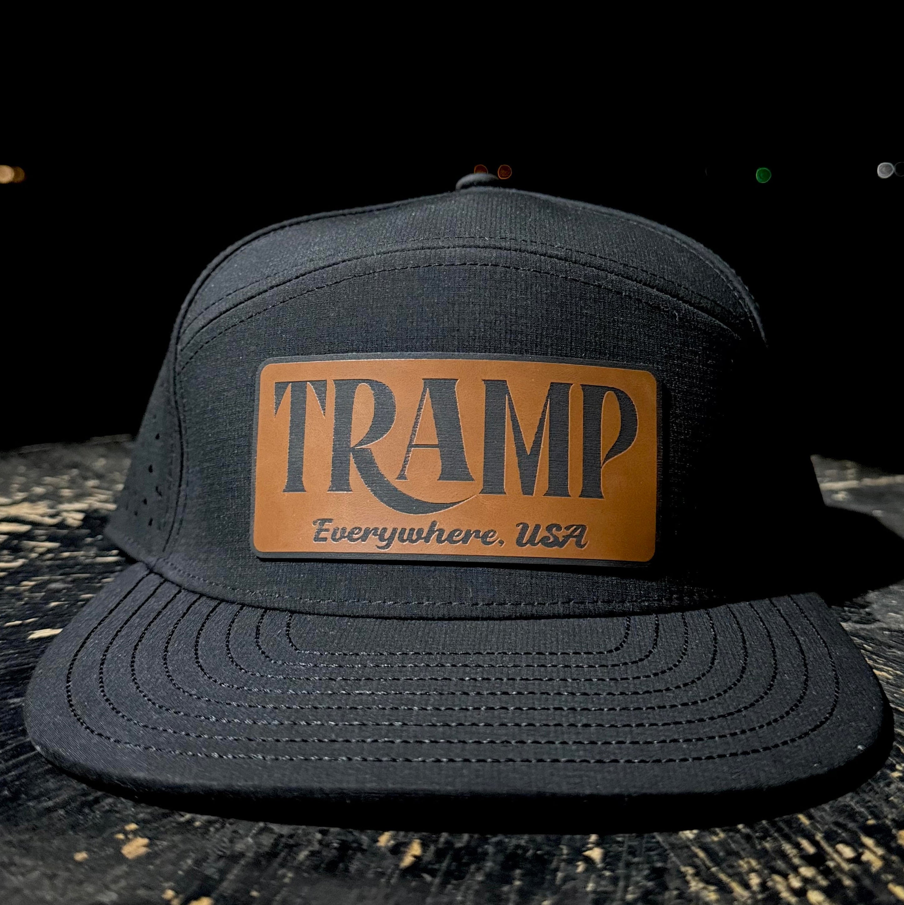 Black cap with a brown leather patch displaying 'TRAMP Everywhere USA' on a dark background.