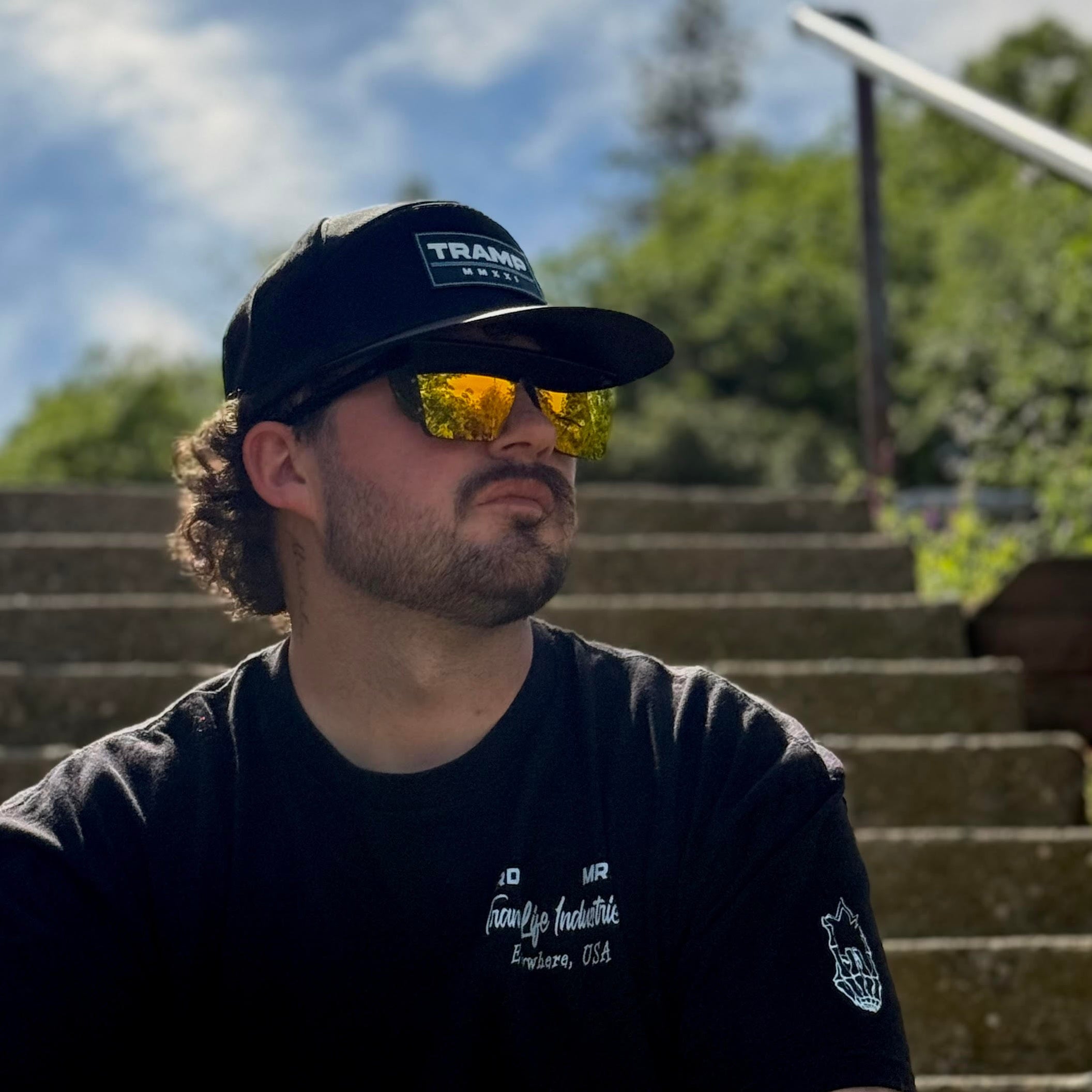 man wearing sunglasses and a hat that say tramp life sitting on steps