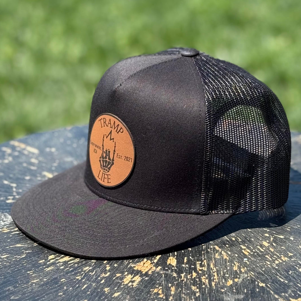 black yupoong snapback with a circular leather patch that has tramp life and a lightning bone hand on it