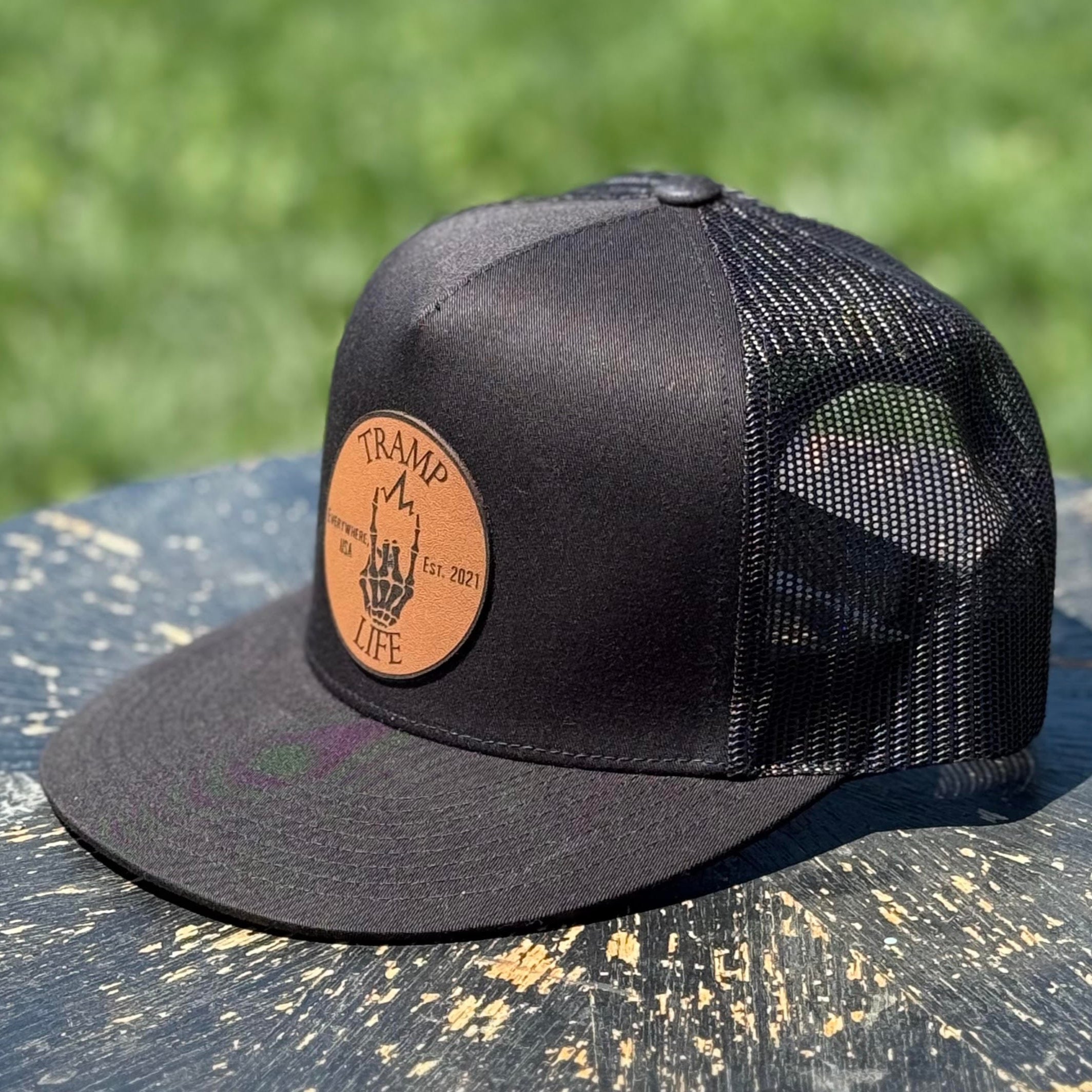 black yupoong snapback with a circular leather patch that has tramp life and a lightning bone hand on it