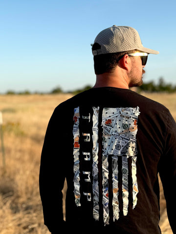 Man wearing a black long-sleeve shirt with a 100 dollar bills in a flag shape with the word tramp written down the middle standing in a field