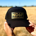 Black cap with 'ND6F' logo held in front of a field