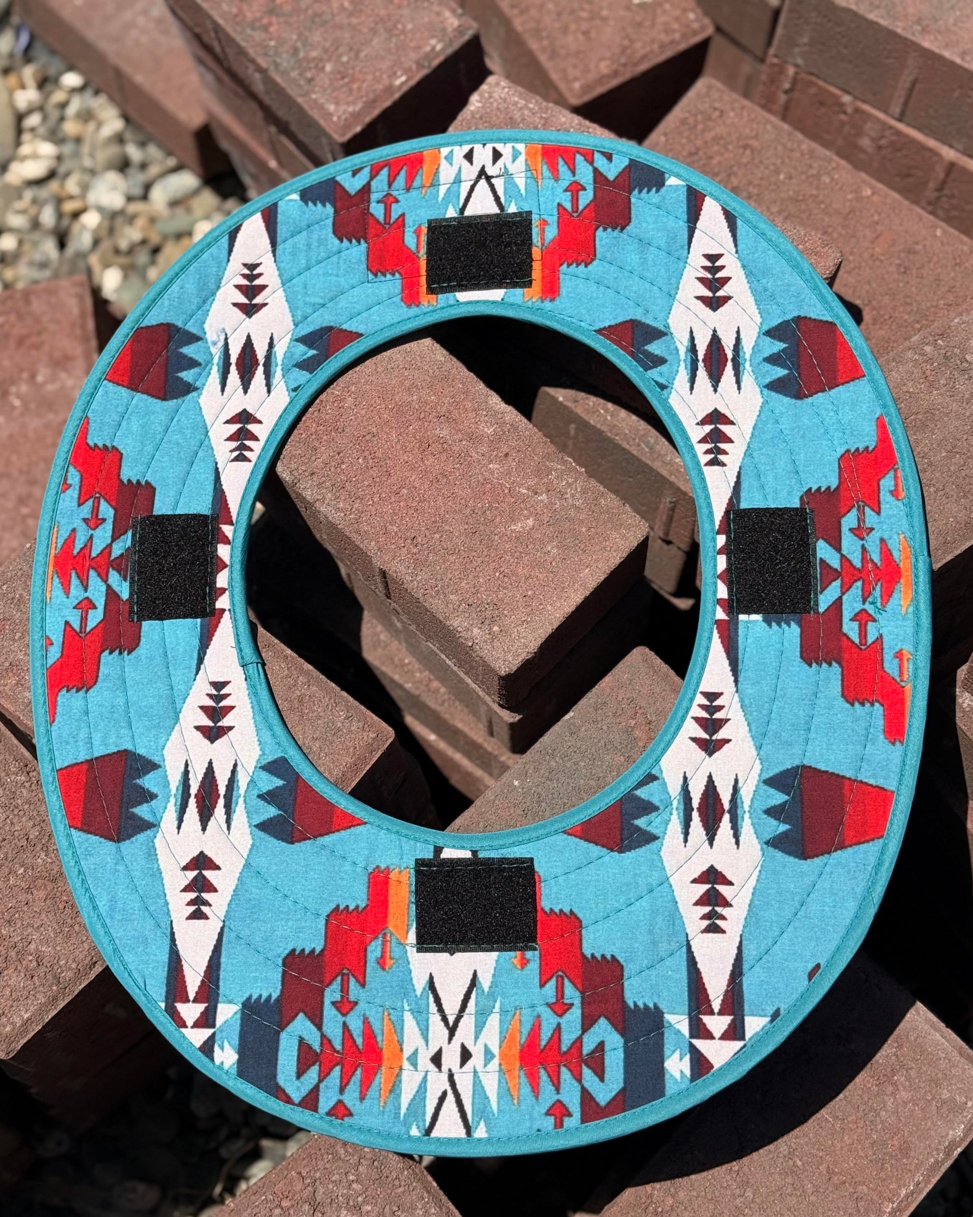 the bottom side of a turquoise sunshade with red, yellow, white and navy accents from tramp life showing the velcro that is sewn into it that shows how the sunshade is attached to the hard hat
