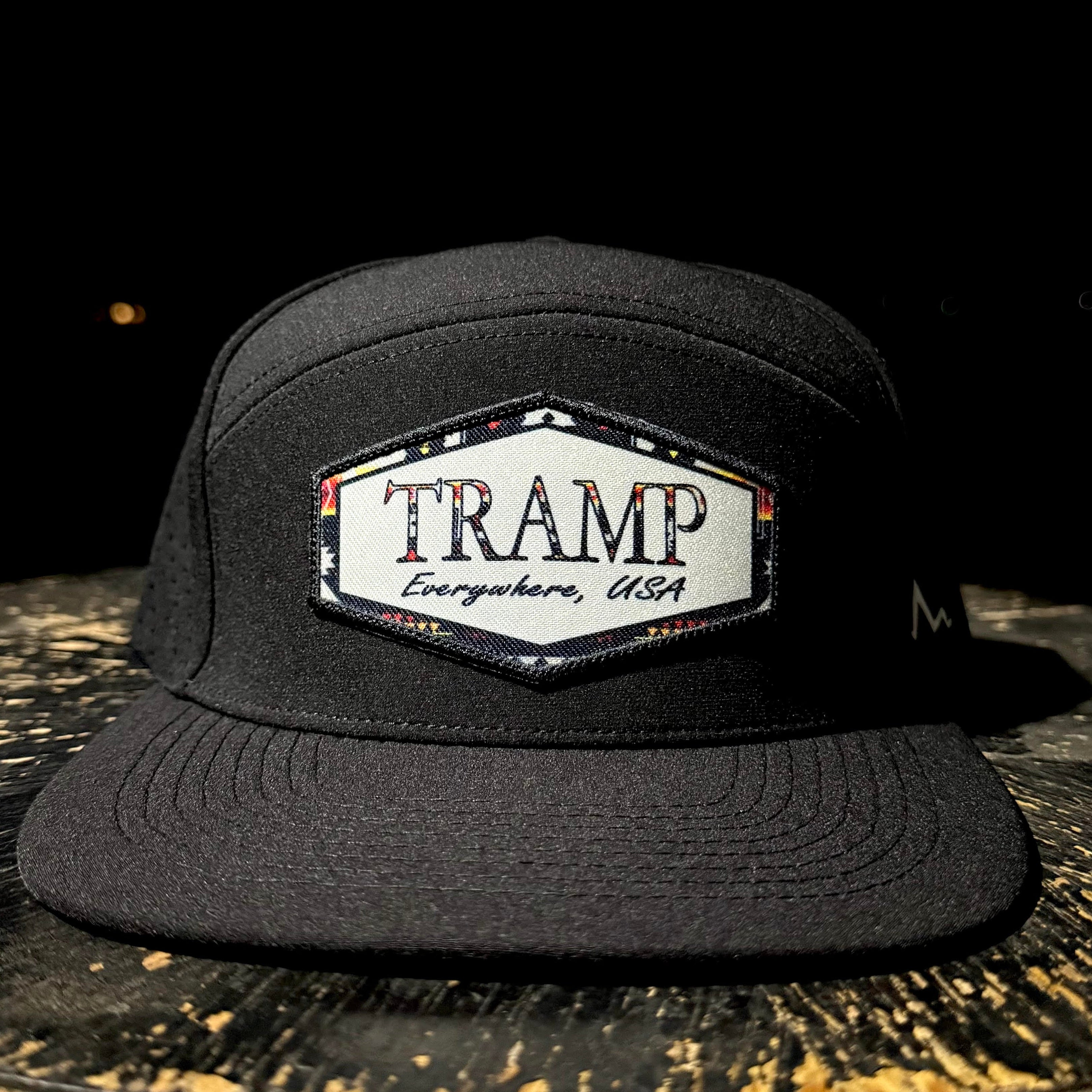 Black cap with 'TRAMP Everywhere, USA' logo on a dark surface