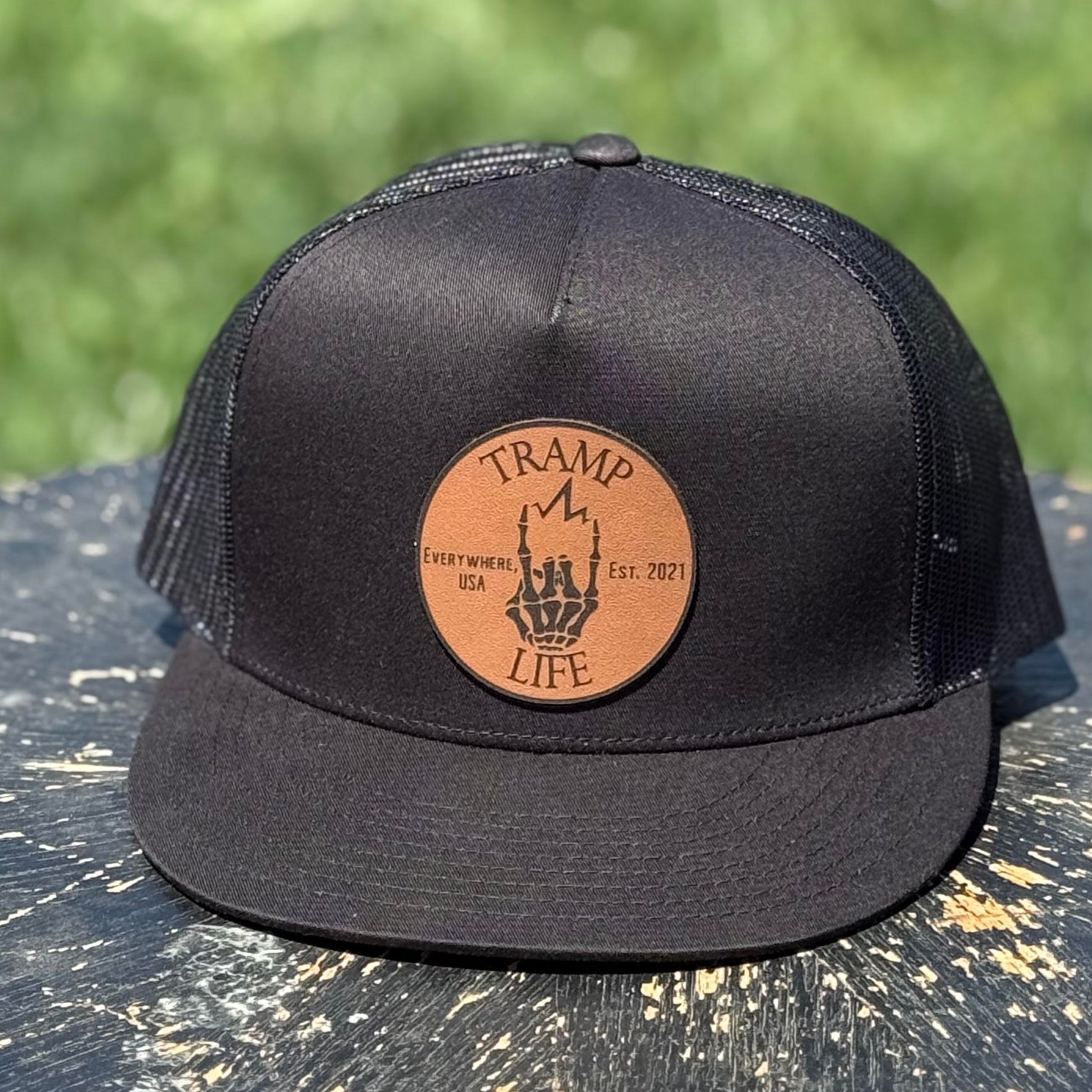 black yupoong snapback with a circular leather patch that has tramp life and a lightning bone hand on it