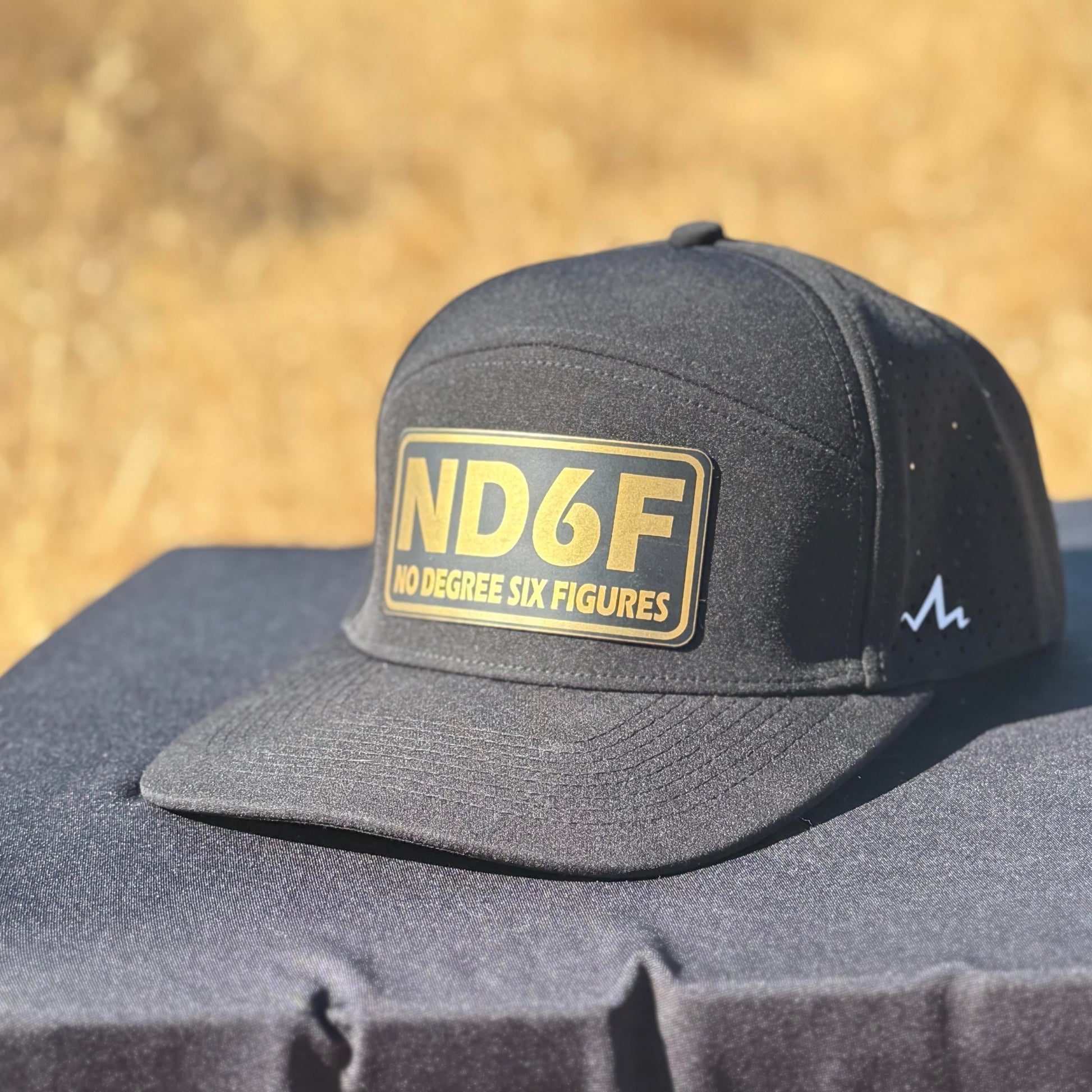the black ND6F gold hat from tramp life on a table in a field
