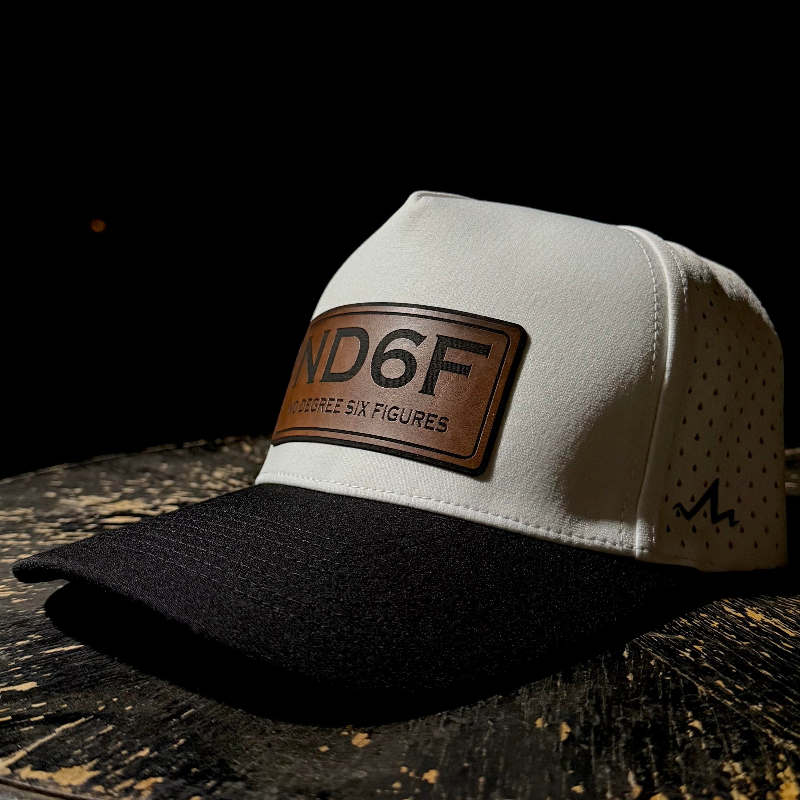 White and black cap with a brown leather patch that says ND6F on a dark surface