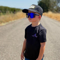 Child wearing a black cap, sunglasses, and black t-shirt with a purple lightning bolt from tramp life  on a rural road.