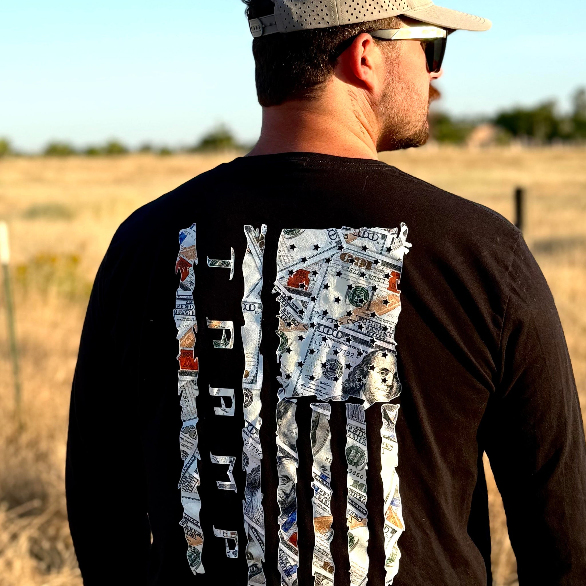 man wearing long sleeve money flag shirt from tramp life standing in a field